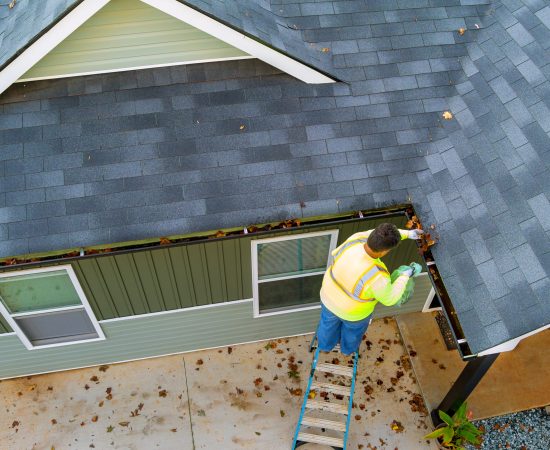 Worker is cleaning clogs in roof gutter drain by picking up dirt, debris, fallen leaves